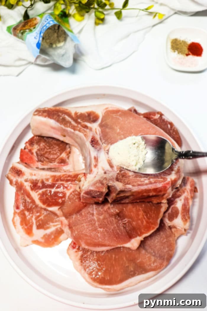 Ultimate Slow Cooker Ranch Pork Chops 4 Raw frozen pork chops on a plate with a spoon adding seasoning, surrounded by spices and a leafy plant.