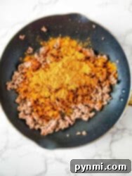 Mouthwatering Slow Cooker Taco Meat 4 Ground meat sizzles in a frying pan, infused with the vibrant flavors of One Pot Taco Pasta seasoning, all set atop a sleek marble countertop.