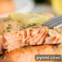 A close-up of grilled salmon with herbs, showcasing a fork revealing its flaky texture, alongside a lemon wedge. Perfectly executed even from frozen, this dish exemplifies how to cook frozen salmon to perfection.