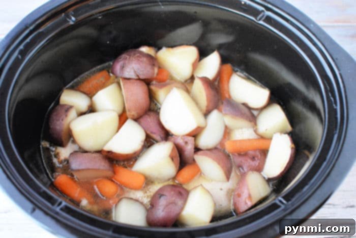 Effortless Slow Cooker Chicken Thighs and Potatoes 7 crockpot chicken and potatoes, garnished with fresh herbs in a white serving bowl, ready to be enjoyed.