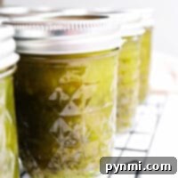 Close-up of sealed glass jars filled with a vibrant canned green pepper jelly, cooling on a metal rack.
