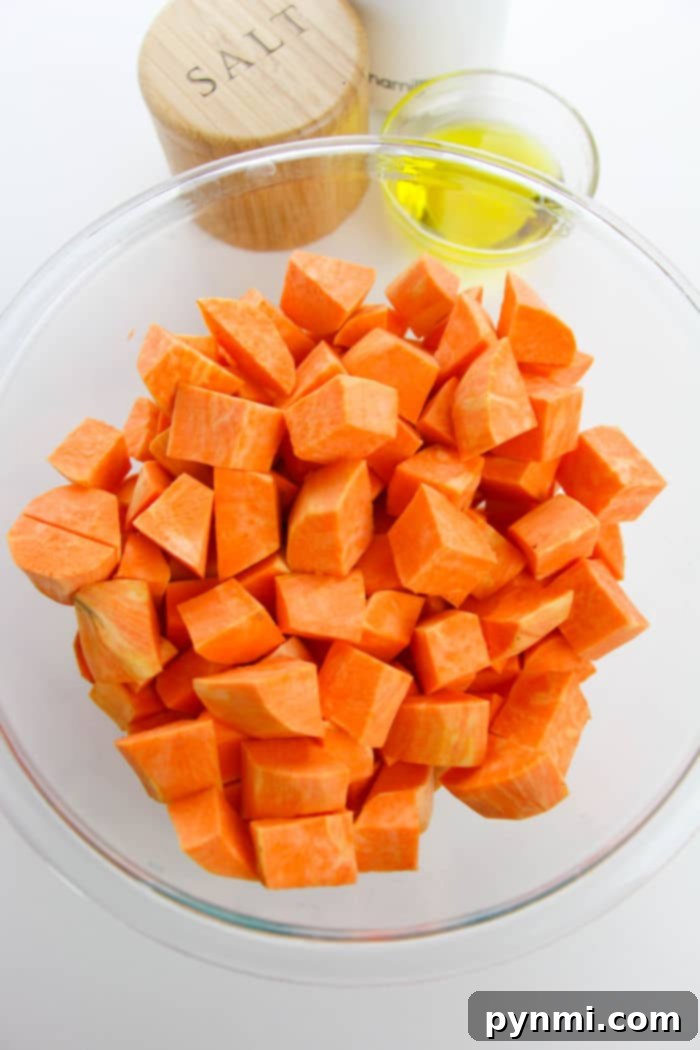 A serving of roasted sweet potato cubes on a white plate, garnished with fresh green herbs, showing the crispy texture.