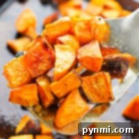 Close-up of roasted sweet potato cubes on a spatula, freshly pulled from the oven, with more pieces scattered on a baking sheet.