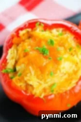 A delicious chicken stuffed red bell pepper with melted cheese and parsley sits elegantly on a black surface, complemented by a charming red-checkered cloth.