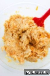 A glass bowl with shredded buffalo chicken dip being mixed by a red spatula, perfect for topping your chicken stuffed bell peppers.