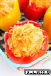 Chicken stuffed red and yellow bell peppers filled with cheese and rice, all nestled in a glass dish.