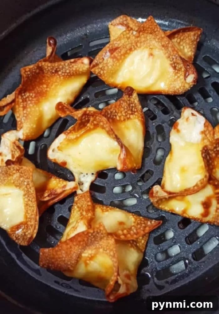 Golden-brown air fryer crab rangoons, fresh out of the air fryer, piled on a serving plate.