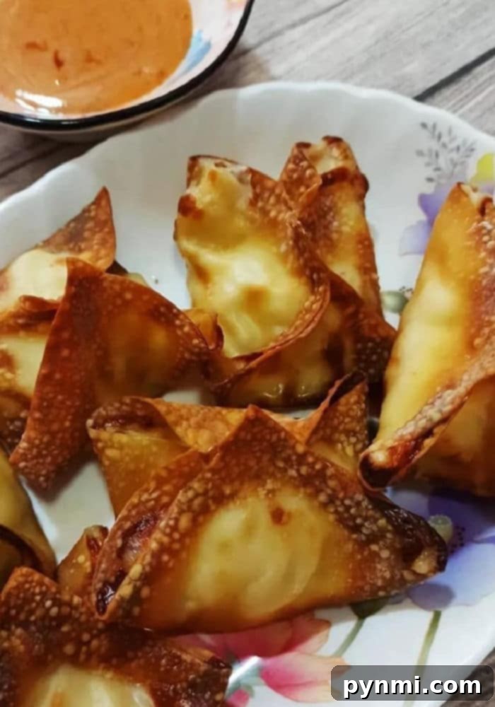 A plate of freshly air-fried crab rangoons with a small bowl of homemade dipping sauce.