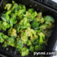 Frozen broccoli, perfectly seasoned, waits in the tray of an air fryer, ready to be cooked to crispy perfection.