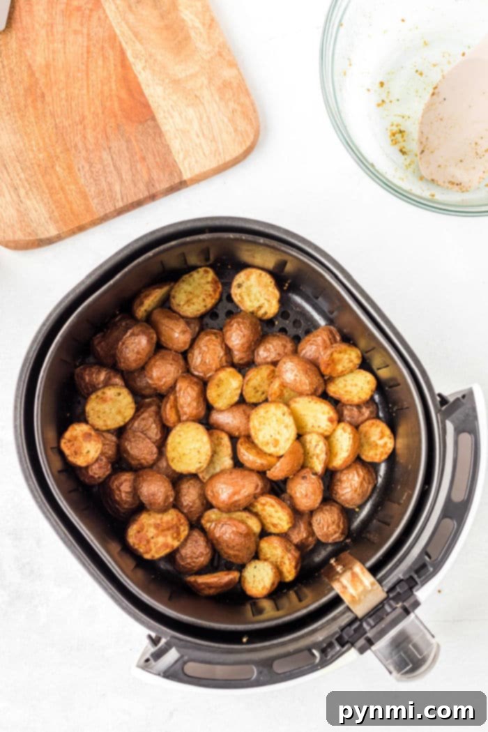 Crispy Air Fryer Potatoes 8 Air fryer basket with perfectly seasoned, crispy air fryer fried potatoes on a white surface.