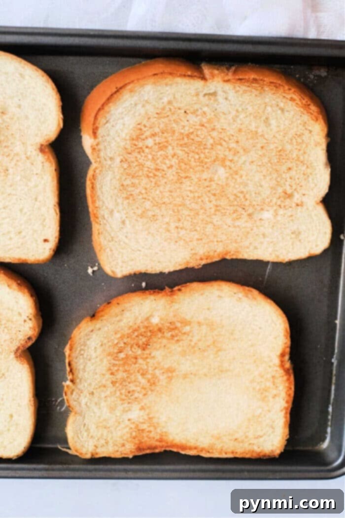 Close-up of golden-brown bread slices toasting on a sheet pan in the oven, emphasizing the even crispness.