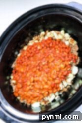 Close-up of a crockpot with venison chili, featuring baked beans, onions, and ground beef.