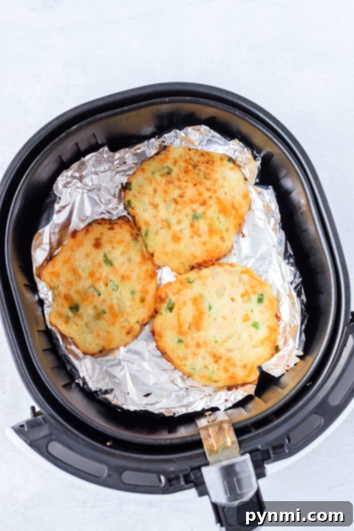 Golden-brown and crispy air fryer potato pancakes are neatly arranged on a sheet of foil inside the air fryer basket, showcasing their perfect texture.