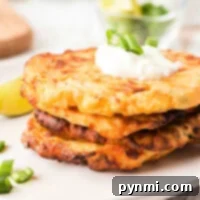 A stack of air fryer potato pancakes topped with sour cream and green onions sits on a plate, accented by a lemon slice in the background.