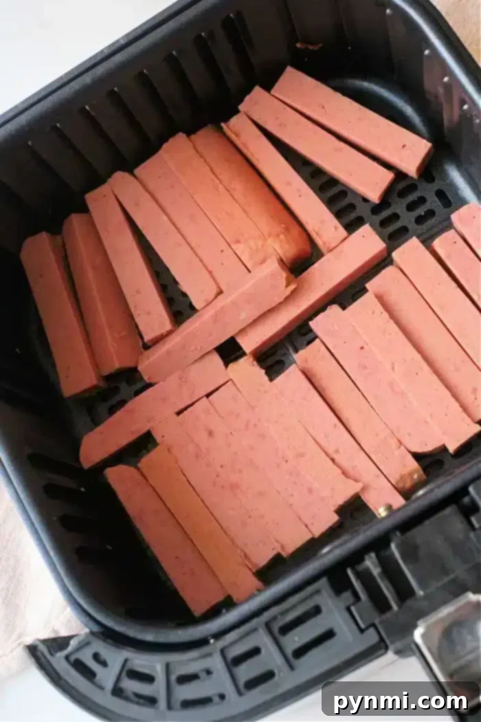 Crispy Air Fryer Spam Fries 6 Sliced pieces of spam are arranged in the basket of an air fryer, ready for cooking
