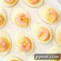 Shrimp deviled eggs are elegantly topped with succulent shrimp and sprinkled with fresh dill, all beautifully arranged on a pristine white plate.