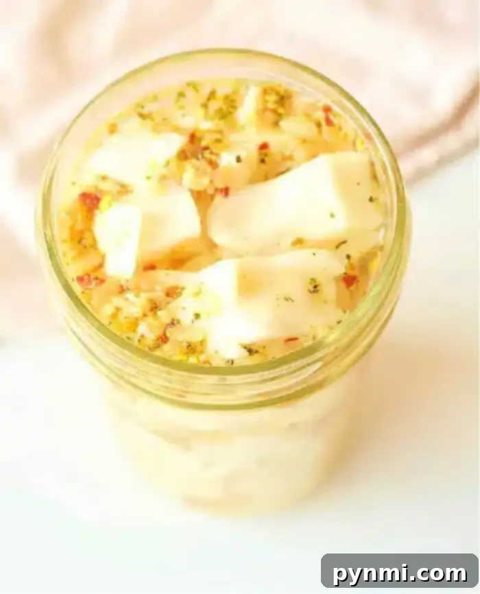Zesty Quick Cabbage Pickle 2 A jar filled with marinated cabbage cubes, topped with fresh herbs and seasoning, sits alongside a vibrant batch of quick-pickled cabbage. The scene is captured from a high angle on a light-colored surface, creating a delightful culinary tableau.