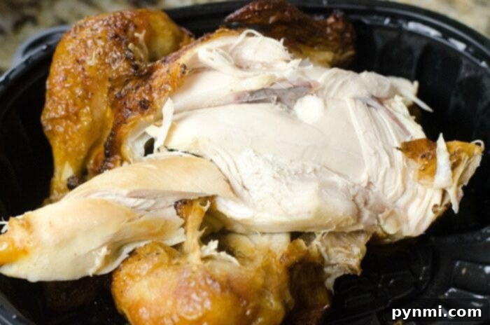 Close-up of a cooked rotisserie chicken in a black plastic container, its golden brown skin enticingly crisp and ready to be shredded.