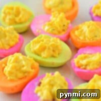 Experience the vibrant hues of Colored Deviled Eggs, featuring bright pink, orange, green, and purple egg whites filled with a sunny yellow egg mixture.