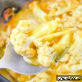 Slow Cooker Cheesy Cauliflower Mac 8 Close-up of a spoon holding Slow Cooker Cheesy Cauliflower, with tender florets smothered in a creamy yellow sauce.