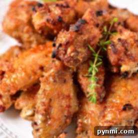 A plate of crispy, golden-brown chicken wings, perfectly suited for reheating in an air fryer, is garnished with fresh herbs.