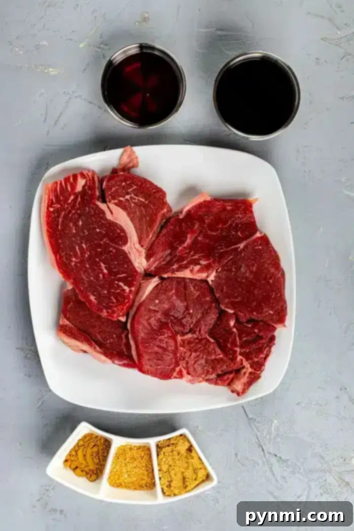 Ultimate Asian Steak Marinade 3 A square white plate with several pieces of raw red beef sits on a textured gray surface, suggesting a perfect base for an Asian steak marinade. Above the plate are two cups, one filled with a dark liquid and the other with a reddish liquid. Below the plate are three small white dishes with various spices.