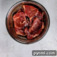 Raw beef pieces, ready for an Asian Steak Marinade, sit enticingly in a metal bowl on a light gray surface.
