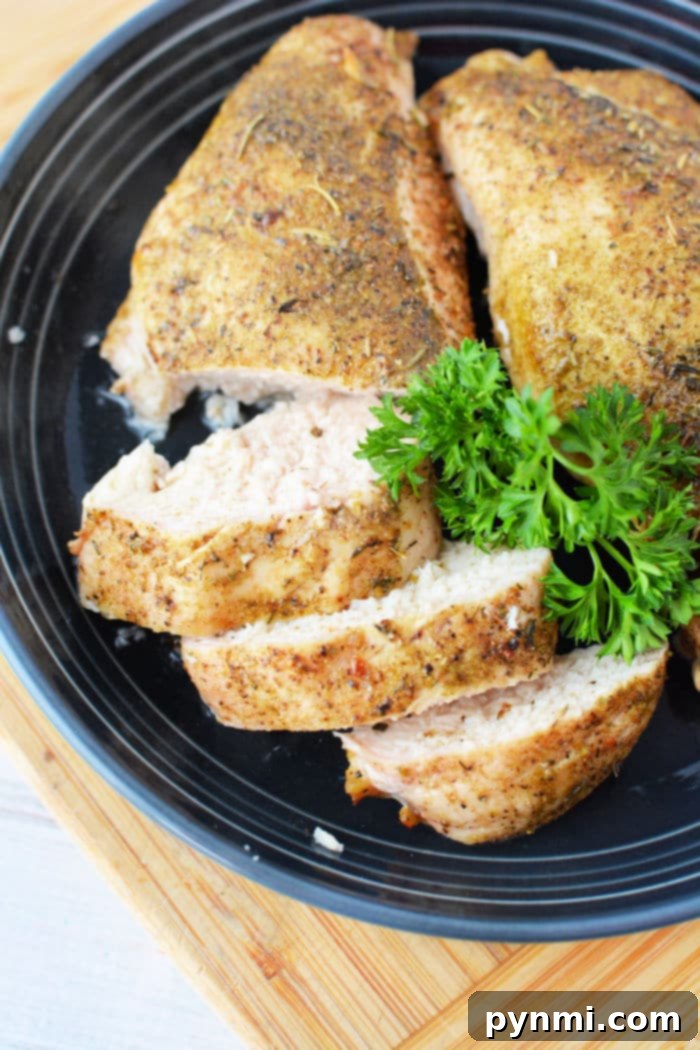 Sliced chicken breast with herbs, roasted to perfection like a frozen chicken breast in the oven, and elegantly garnished with parsley on a sleek black plate.