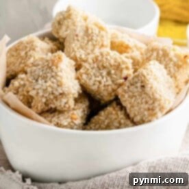 A white bowl filled with sesame-covered tofu nuggets rests on a cloth napkin.
