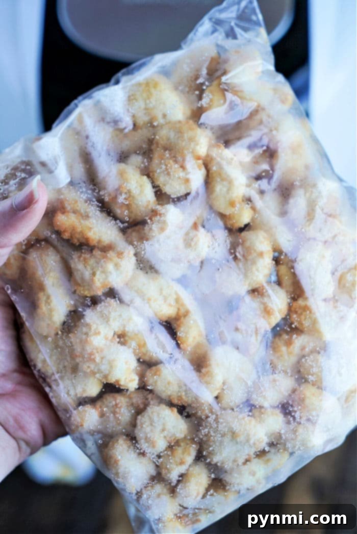 Crispy Air Fryer Popcorn Shrimp 9 A hand holds a clear plastic bag filled with frozen breaded chicken nuggets, reminiscent of frozen popcorn shrimp ready for the air fryer. The nuggets are covered with frost, indicating they are icy and perfectly preserved. The background is slightly blurred and indistinct.