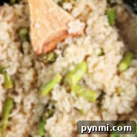 Close-up of creamy slow cooker risotto, with asparagus pieces being stirred gently with a wooden spoon.