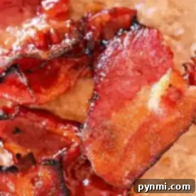Close-up of crispy, cooked bacon slices on a brown surface. The bacon appears glossy and caramelized, reminiscent of air fryer maple candied bacon.