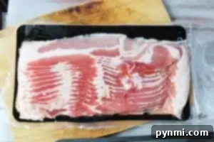 A sealed package of uncooked bacon strips is placed on a wooden cutting board.
