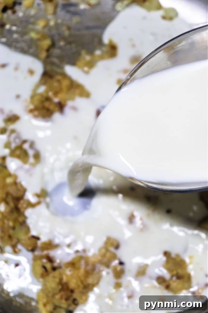 Milk being poured into a saucepan of smooth, simmering chicken gravy, indicating the final stages of preparation.