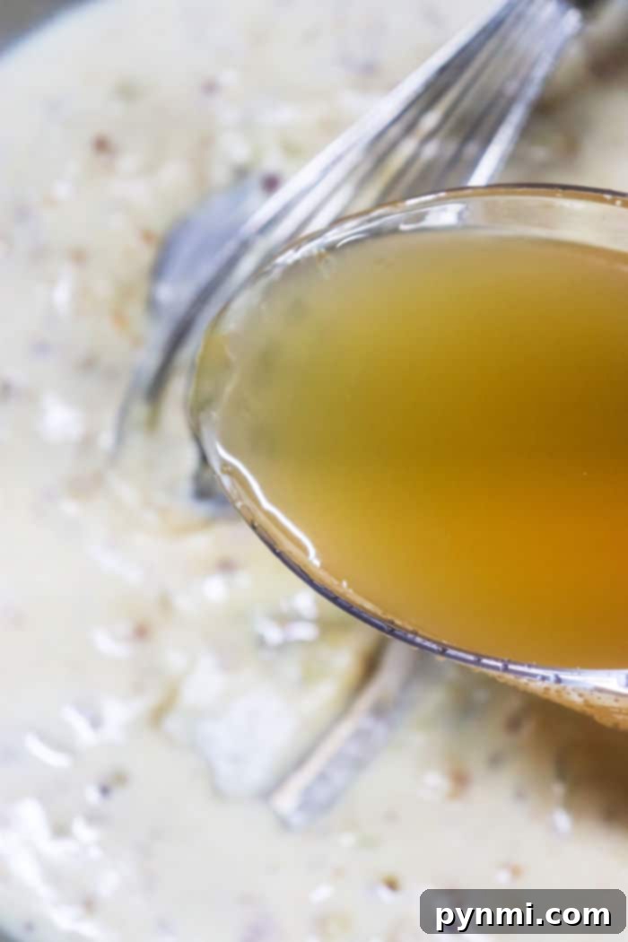 A close-up of thick, homemade chicken gravy in a saucepan, being stirred with a whisk.