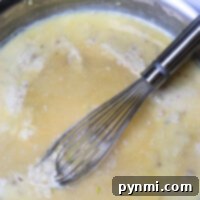 A whisk gently stirs creamy chicken gravy in a pan, highlighting its smooth texture.