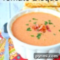 A bowl of creamy tomato bisque, crafted from an easy tomato bisque recipe, is garnished with herbs and sits beside a spoon on a colorful cloth.