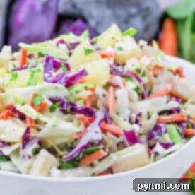 A bowl of colorful Hawaii Coleslaw with green and purple cabbage, carrots, pineapple, and fresh herbs.