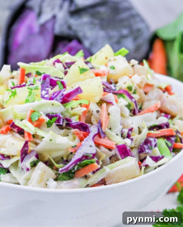 A vibrant and fresh bowl of Hawaiian coleslaw with green and purple cabbage, carrots, pineapple, and fresh herbs, ready to be served.