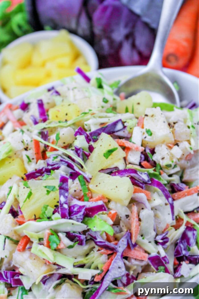 A beautifully arranged setting featuring a bowl of vibrant Hawaii coleslaw with colorful cabbage, carrots, and juicy pineapple chunks, accompanied by a spoon and fresh ingredients, inviting a delightful meal.