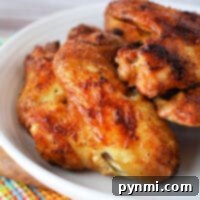 Close-up of whole chicken wings, perfectly crisped in an air fryer, resting on a white plate atop a colorful checkered cloth.