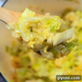 A wooden spoon holding stewed cabbage above a pot filled with more tender, cooked cabbage.
