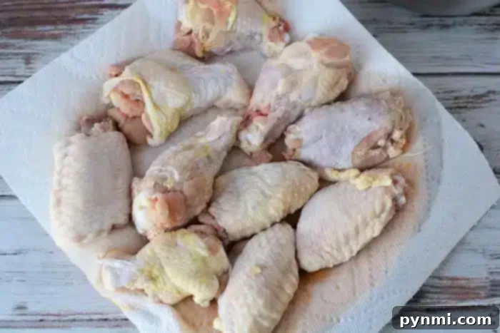 Crispy Air Fryer Wings Baking Powder Secret 4 A collection of raw chicken wings and drumsticks are laid out on a white paper towel on a rustic, white wooden table. The fresh chicken pieces are ready for preparation or cooking, and would be perfect as air fryer chicken wings when seasoned with a touch of baking powder.