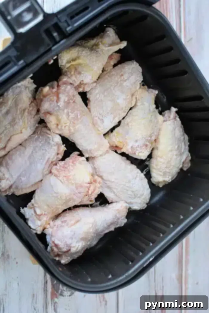 Crispy Air Fryer Wings Baking Powder Secret 6 A close-up of raw, seasoned chicken wings dusted with baking powder, placed inside a black air fryer basket and ready for cooking. The countertop beneath reveals a light-colored surface with a faint wood grain pattern.