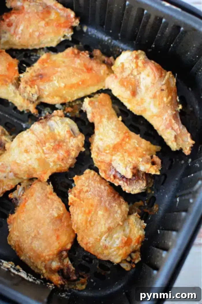Crispy Air Fryer Wings Baking Powder Secret 9 Eight pieces of crispy, golden-brown chicken wings are shown inside a black air fryer basket. The wings have a slightly uneven, textured surface, indicating they are well-cooked and well-seasoned. Thanks to the addition of baking powder, these air fryer chicken wings achieve their delightful crunch.