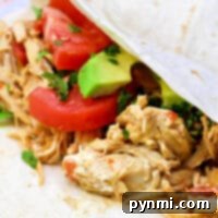 A close-up of a soft taco reveals pressure cooker chicken, infused with flavor, alongside sliced tomatoes, avocado, and cilantro on a white tortilla.