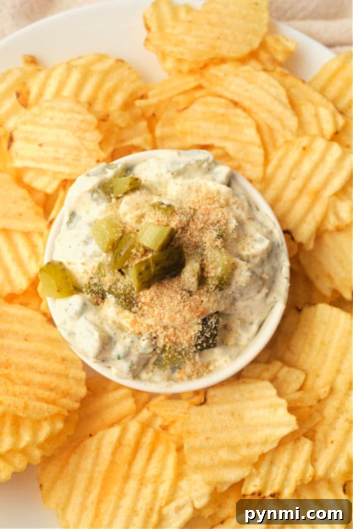A bowl of creamy pickle dip with a rustic wooden spoon, surrounded by an array of crunchy chips and fresh dill sprigs, ready for serving at a party.