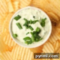 A bowl of creamy Lawson's Chip Dip, topped with chopped green onions, is surrounded by crispy potato chips.