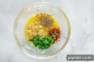 A glass bowl with melted butter, chopped garlic, parsley, red pepper flakes, and Italian herbs, ready for mixing to make garlic bread.