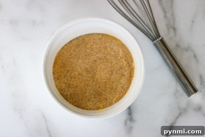 A white bowl filled with Lawry's seasoned salt next to a metal whisk on a marble surface, ready for use.